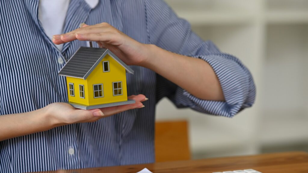 Woman hands sheltering small house model.