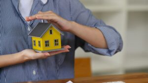 Woman hands sheltering small house model.