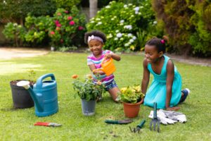 Smiling african american girl kneeling by sister watering plant at garden