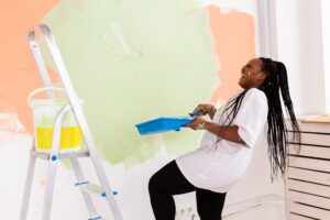 Smiling african american woman painting interior wall of home. Renovation, repair and redecoration